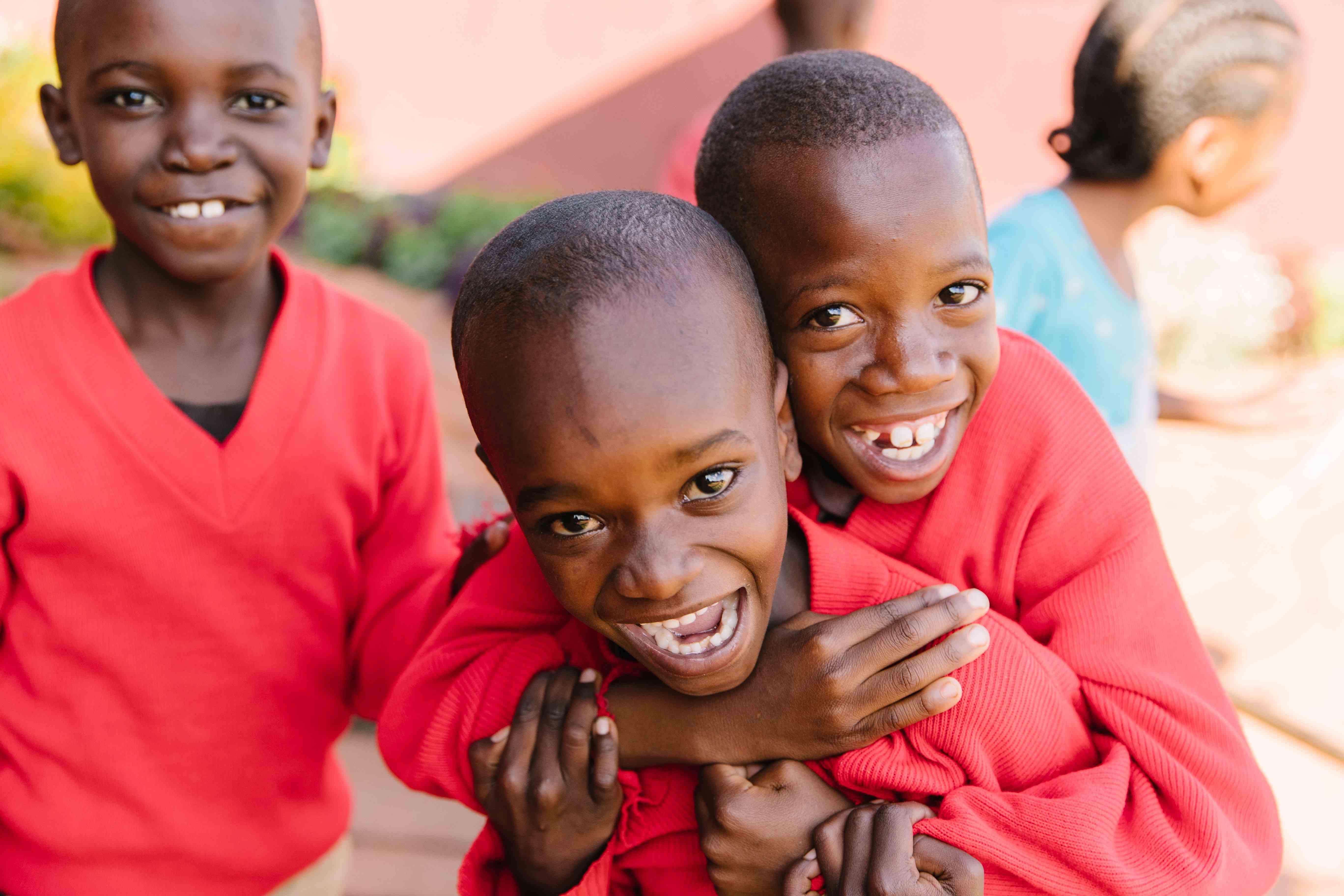 Three boys in red sweaters smiling and hugging